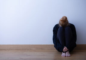 Picture of a sad teenage girl suffering from loneliness, sitting alone on the floor, copy space on empty wall