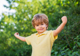 Child outdoors in nature. Happy child. Funny baby boy isolated on a background of green trees. Smiling child boy. Cheerful cheerful kid. Happy children kid boy with hands up